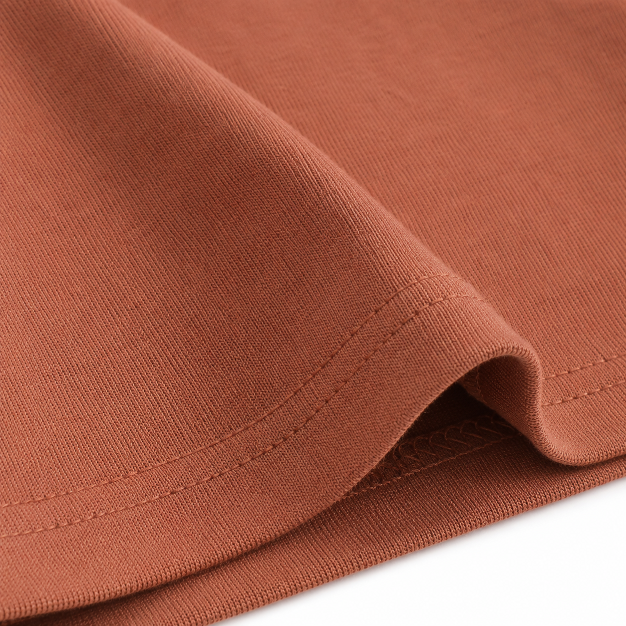 Close-up of the hem stitching and cotton fabric on the terracotta long sleeve kids shirt.