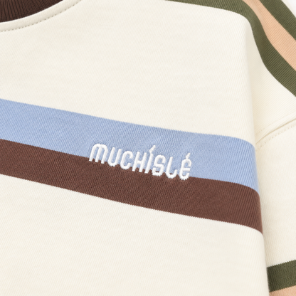 Close-up of the small white embroidered chest detail on the cream multicolor striped T-shirt.