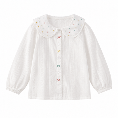 Front view of a white girls cotton blouse with a scalloped dotted collar, long sleeves and colorful bow details.