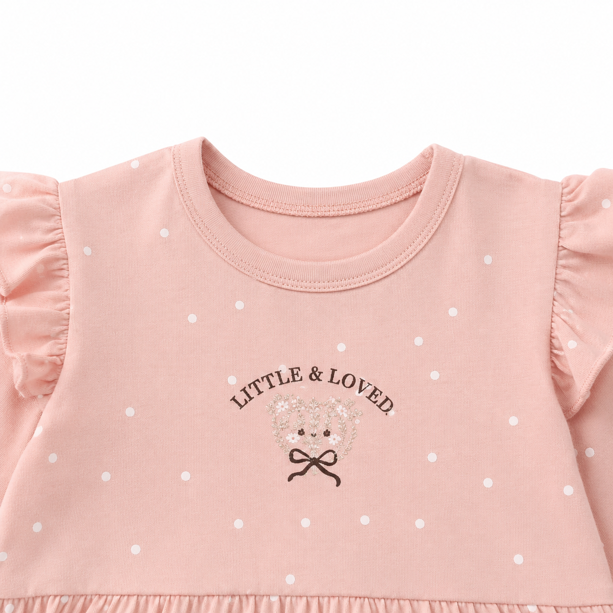 Close-up of the Little & Loved chest graphic and white polka dots on the blush pink girls cotton top.