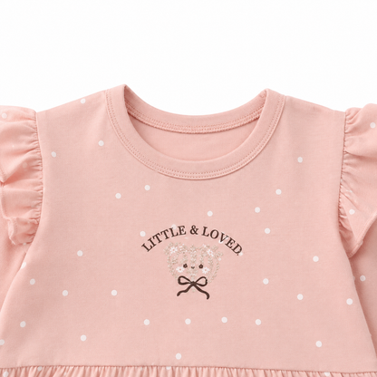 Close-up of the Little & Loved chest graphic and white polka dots on the blush pink girls cotton top.