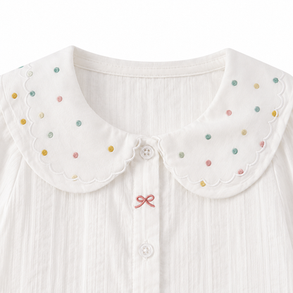 Close-up of the scalloped collar with multicolor dot details on the white girls cotton blouse.