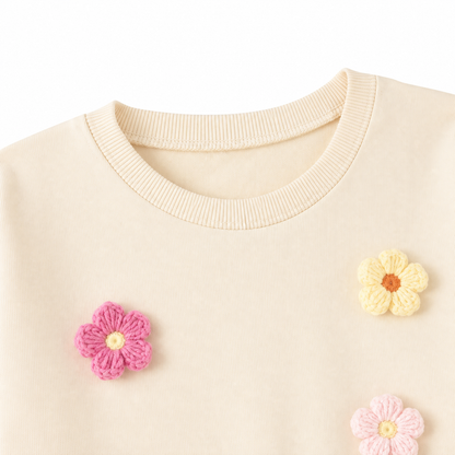Close-up of the neckline and flower applique detail on the cream girls top.