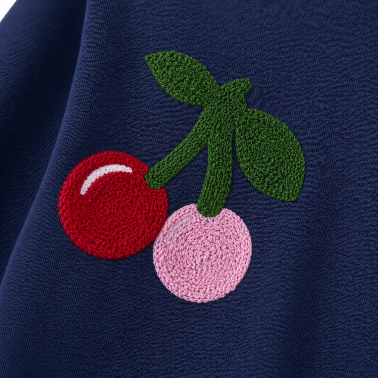 Close-up of the red and pink cherry motif on the navy girls dress.