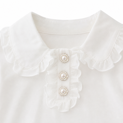 Close-up of the front ruffle placket and decorative button detail on a white girls top.