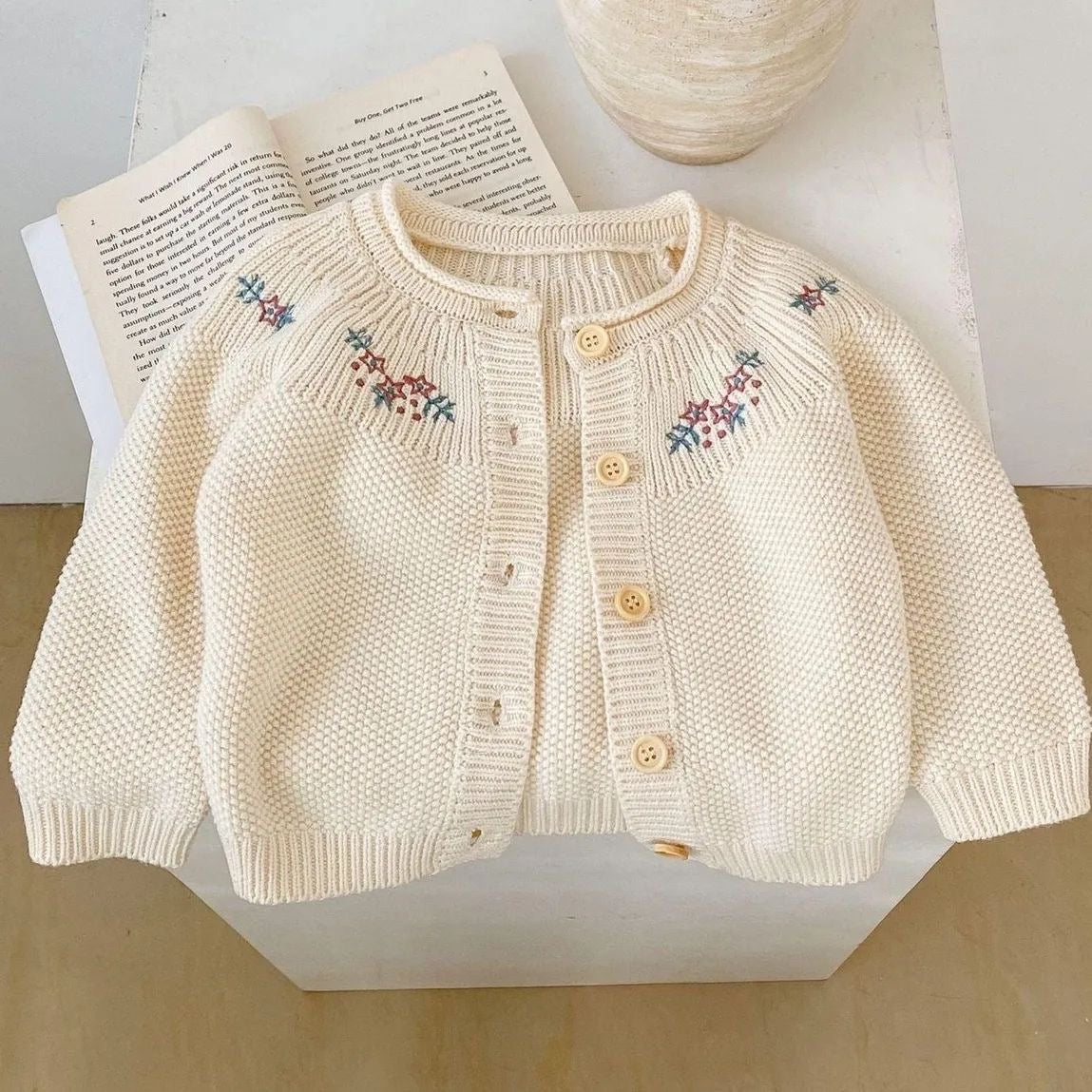 Close-up of the floral embroidery detail on a cream girls cardigan.