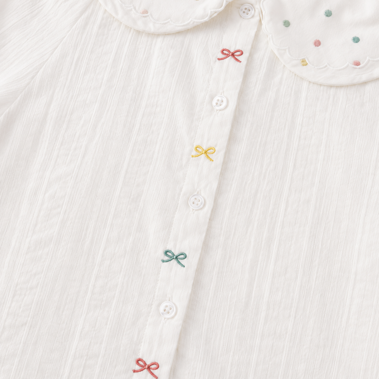 Close-up of the front buttons and colorful embroidered bow details on the white girls blouse.