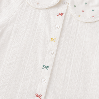 Close-up of the front buttons and colorful embroidered bow details on the white girls blouse.