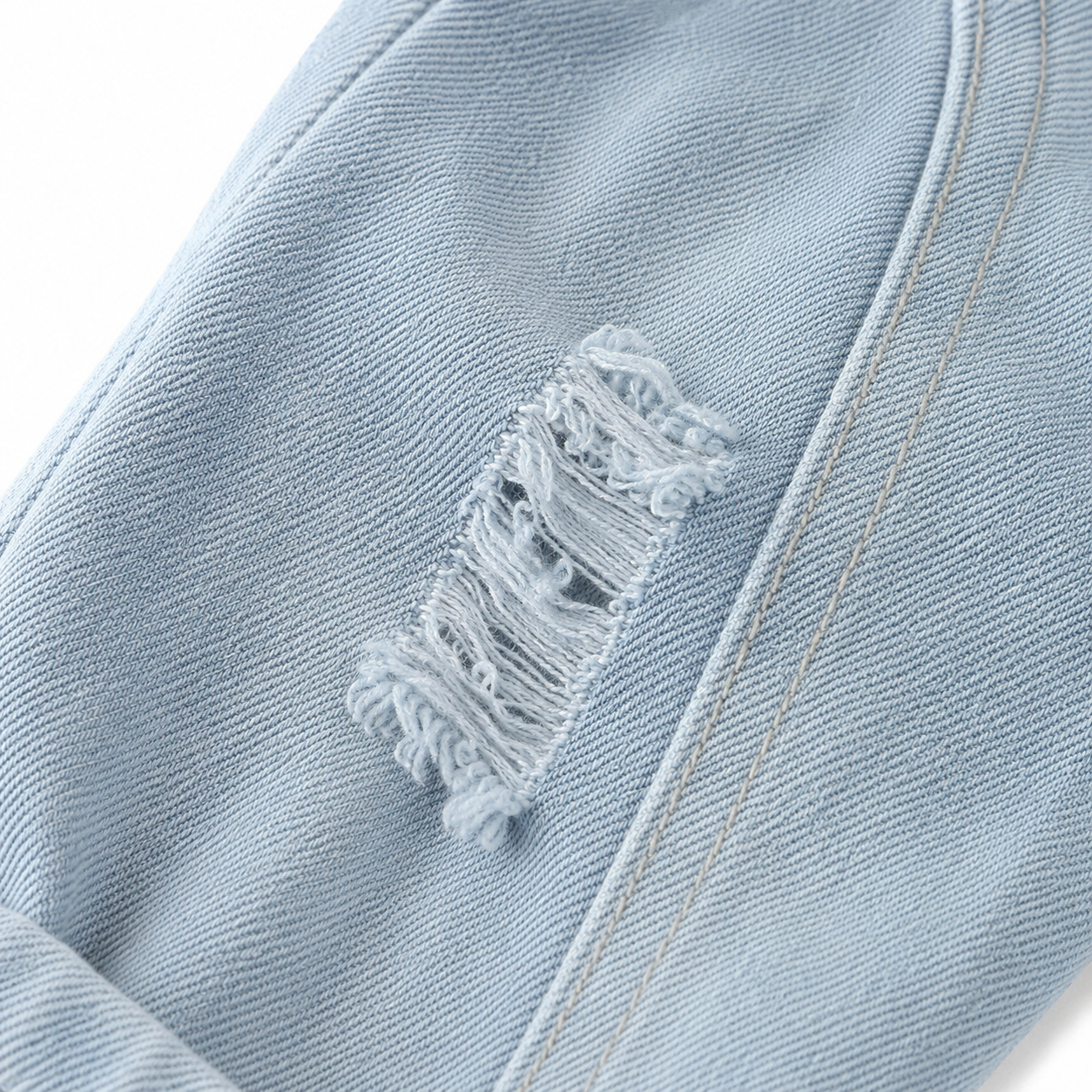 Close-up of distressed denim detail on boys light wash jeans.