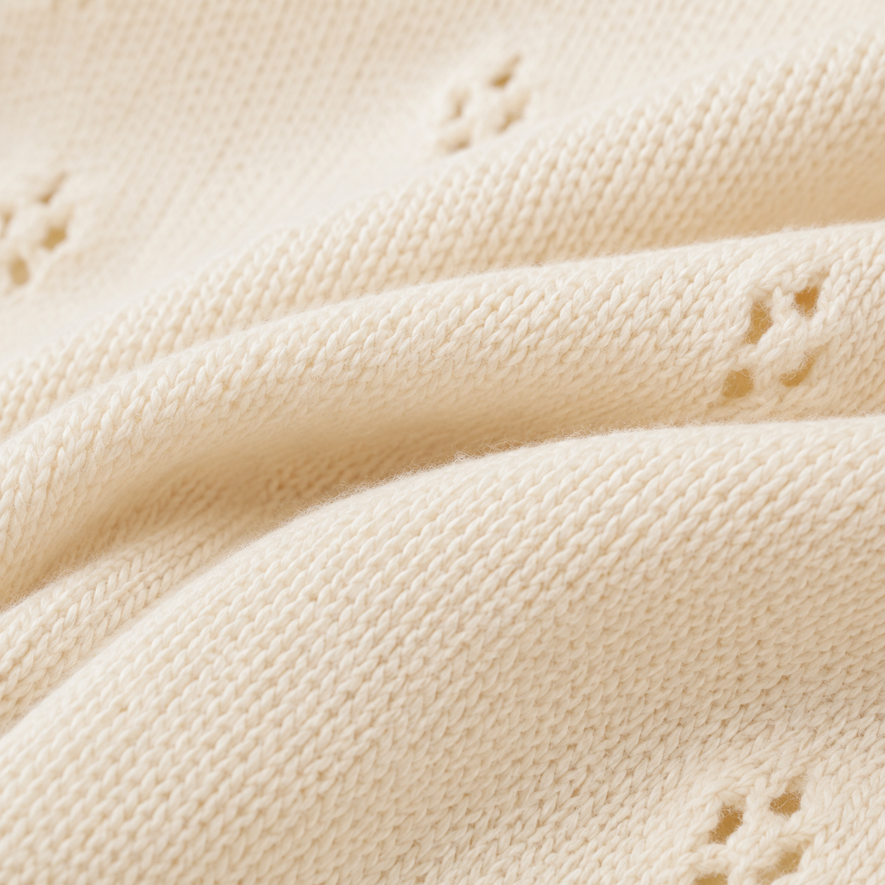 Macro view of the soft cream cotton knit texture and small openwork eyelet pattern.