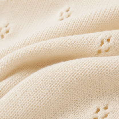 Macro view of the soft cream cotton knit texture and small openwork eyelet pattern.