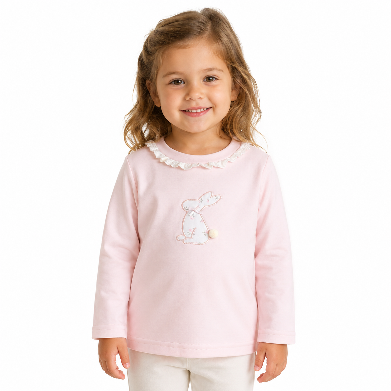 Girl model wearing the Blush Pink cotton long sleeve ruffle collar top with bunny embroidery with a small pom-pom tail detail on a white studio background.