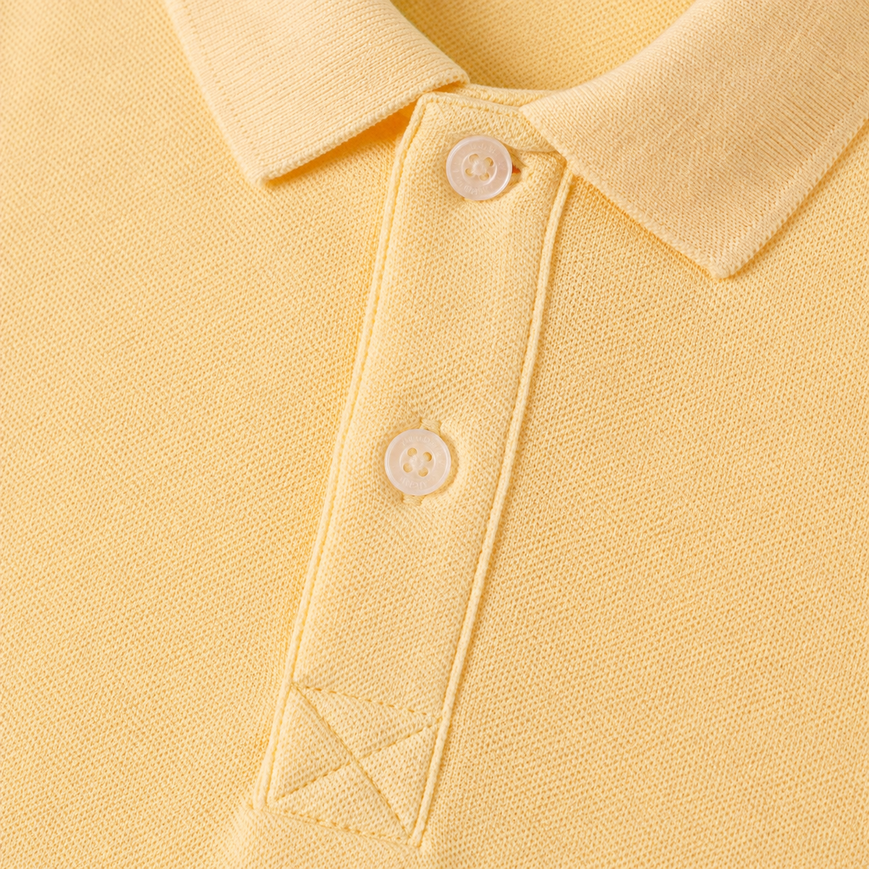 Close-up of the collar and button placket construction on the butter yellow long sleeve polo.
