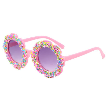 Pink girls sunglasses with flower-shaped frame, candy sprinkle details, and UV400 lenses.