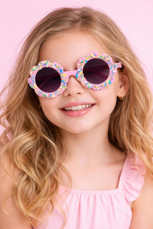 Girl wearing pink candy bloom kids sunglasses with flower frame and colorful sprinkle details.
