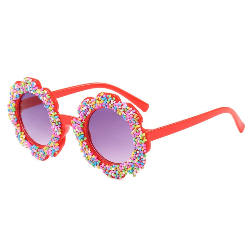 Red kids sunglasses with round flower frame, colorful candy sprinkle trim, and UV400 tinted lenses.