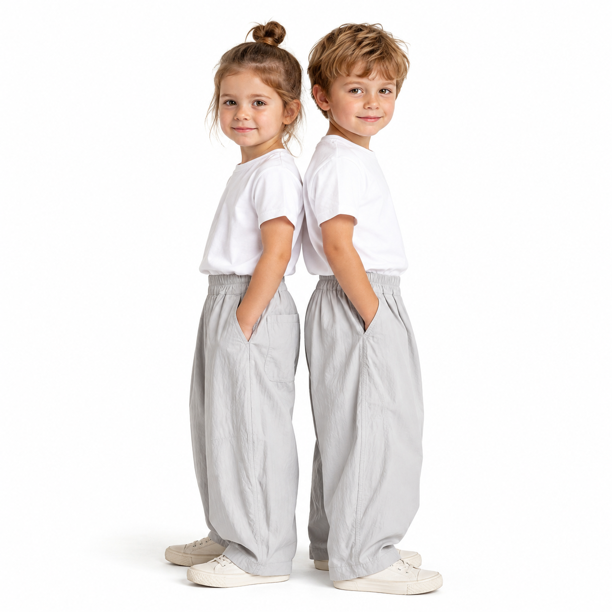 Girl and boy models wearing the light gray kids balloon pants with simple white tops.