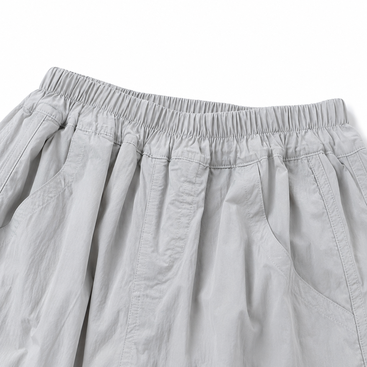 Close-up of the gathered elastic waistband and pleated front detail on the light gray balloon pants.