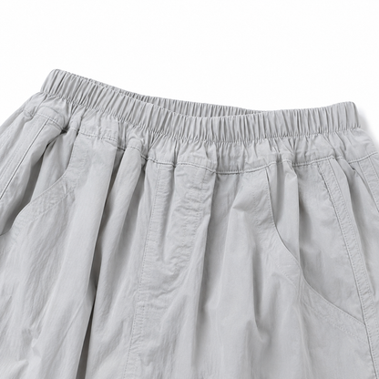 Close-up of the gathered elastic waistband and pleated front detail on the light gray balloon pants.