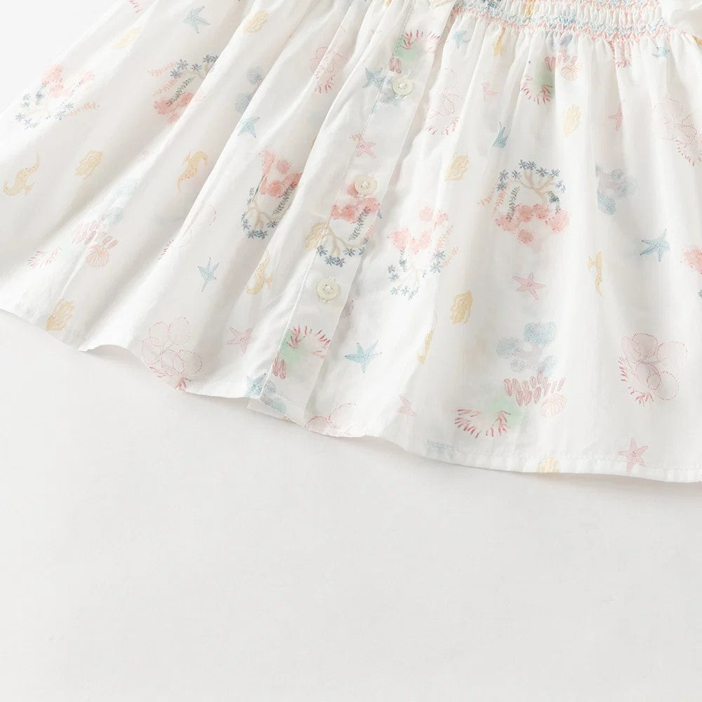 Close-up of the gathered hem, front buttons and pastel ocean print on the smocked girls blouse.