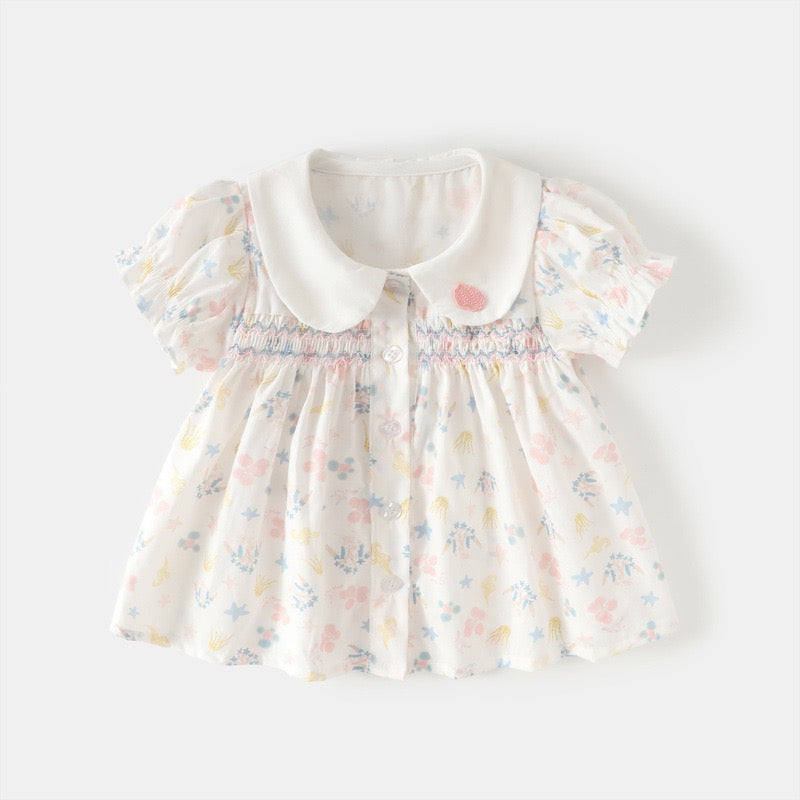 Front view of a white smocked girls cotton blouse with pastel sea life print, Peter Pan collar and puff sleeves.