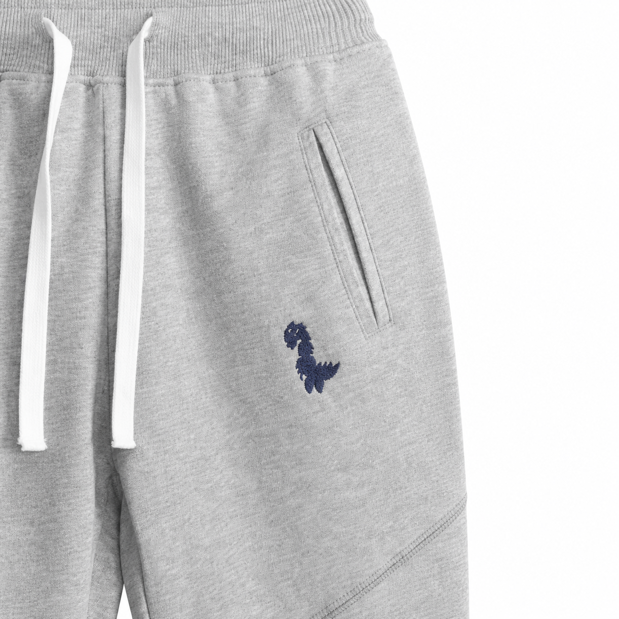 Close-up of the small dinosaur embroidery and side pocket on the light gray kids pants.