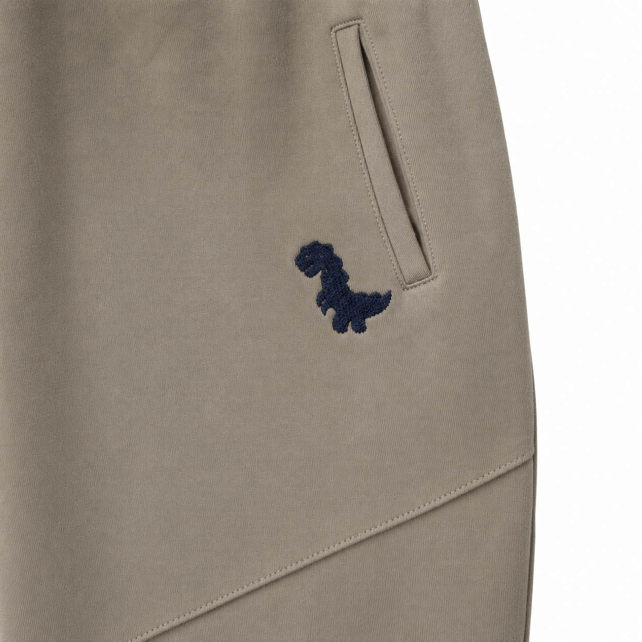 Close-up of the small dinosaur embroidery and side pocket on the taupe kids pants.