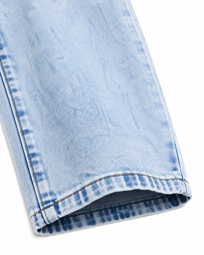 Close-up of the denim fabric, seam, and pant leg hem on the light blue denim jeans.