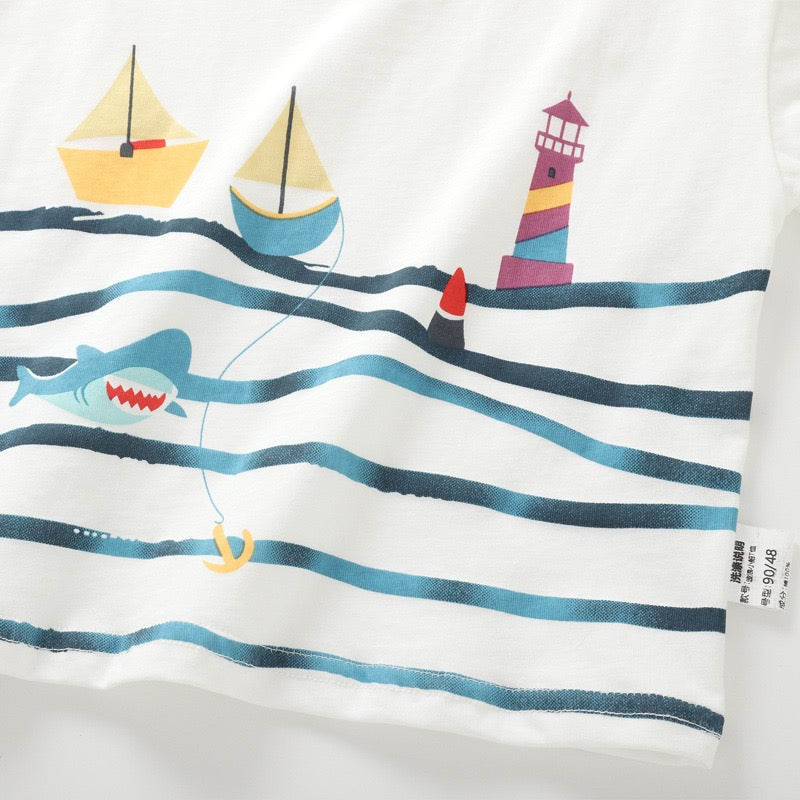 Close-up of the sailboat, lighthouse, ocean wave and shark graphic on the white kids T-shirt.