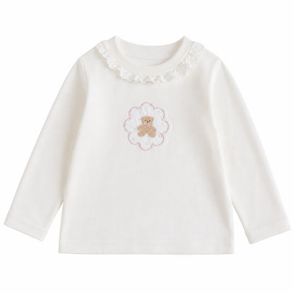 Front flat lay of the Ivory girls cotton long sleeve top with ruffle collar and teddy bear framed by a flower outline on a white background.