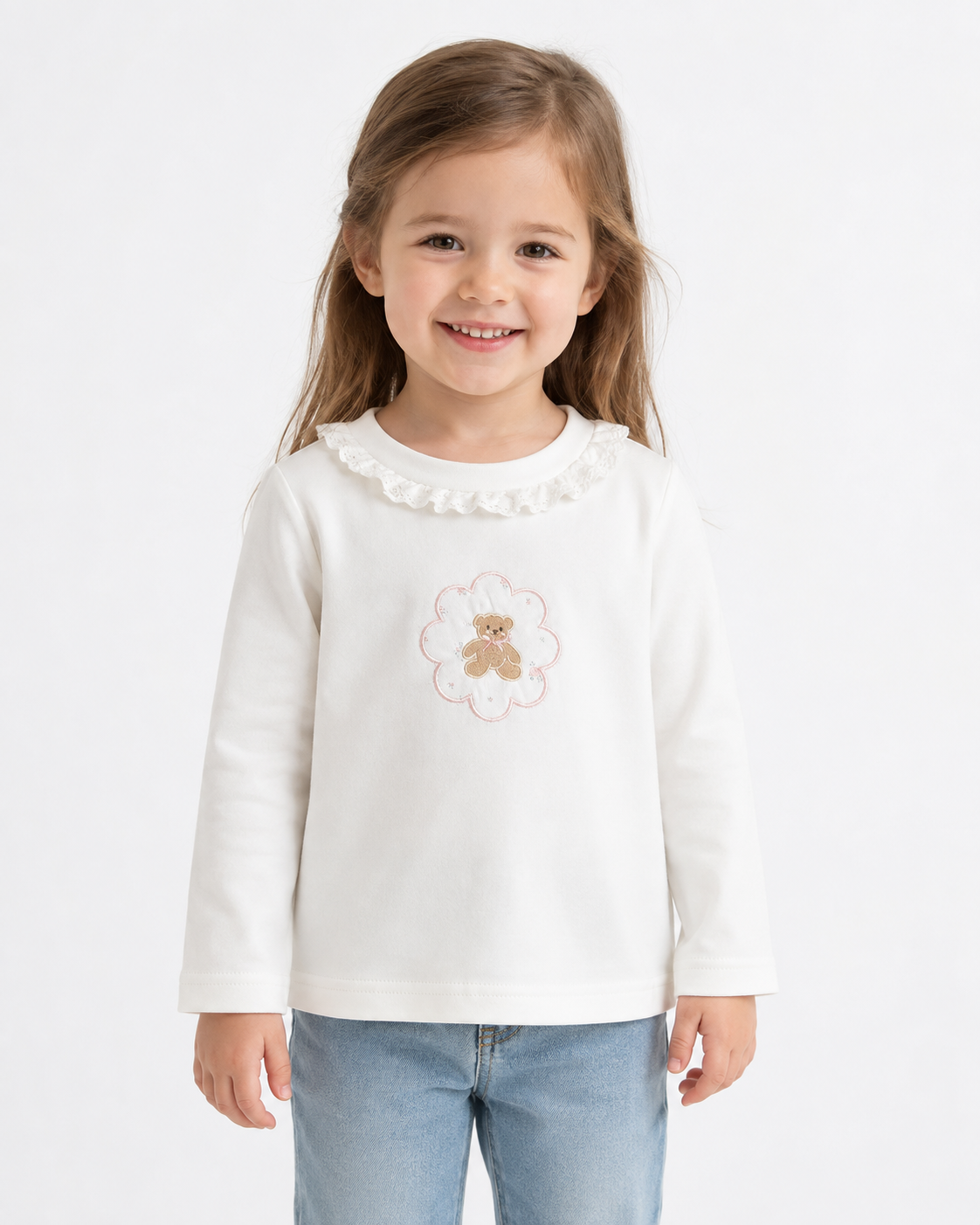 Girl model wearing the Ivory cotton long sleeve ruffle collar top with teddy bear framed by a flower outline on a white studio background.