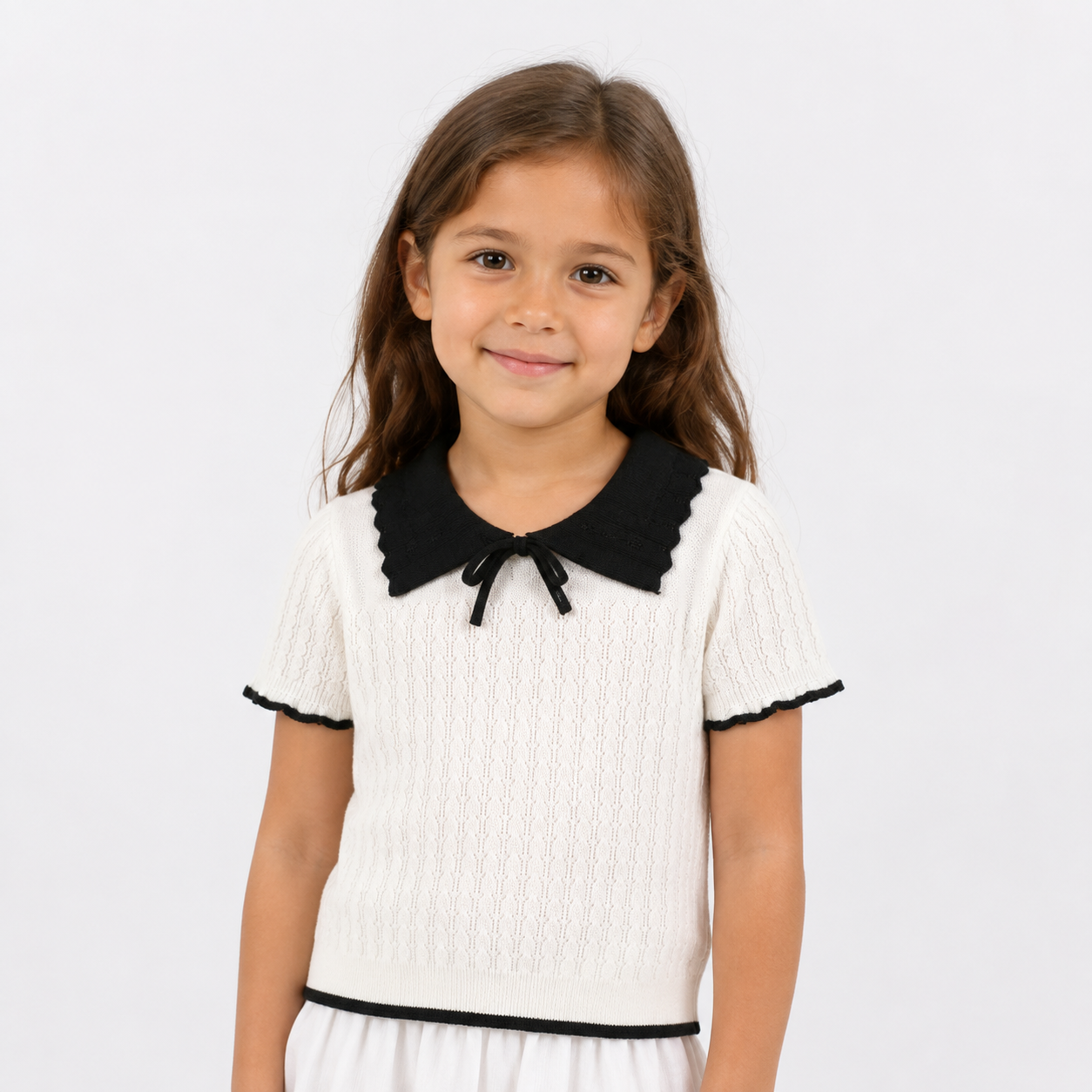 Girl model wearing an ivory bow collar knit top with black contrast trim on a white background.