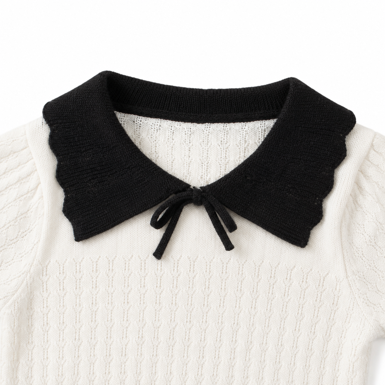 Close-up of the black contrast collar and neckline construction on an ivory girls knit top.