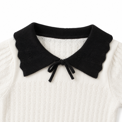 Close-up of the black contrast collar and neckline construction on an ivory girls knit top.