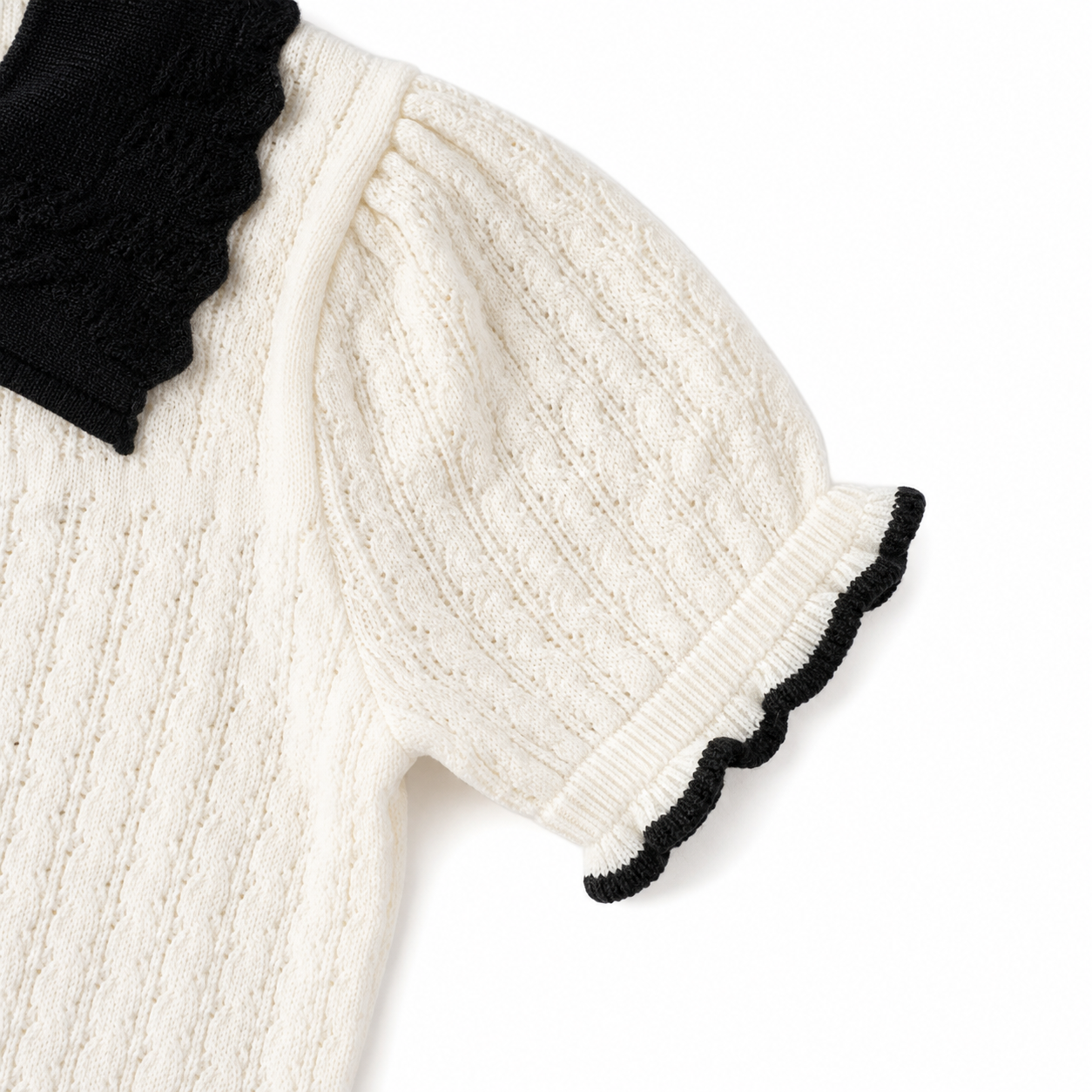 Close-up of the textured short sleeve and black edge trim on an ivory girls knit top.