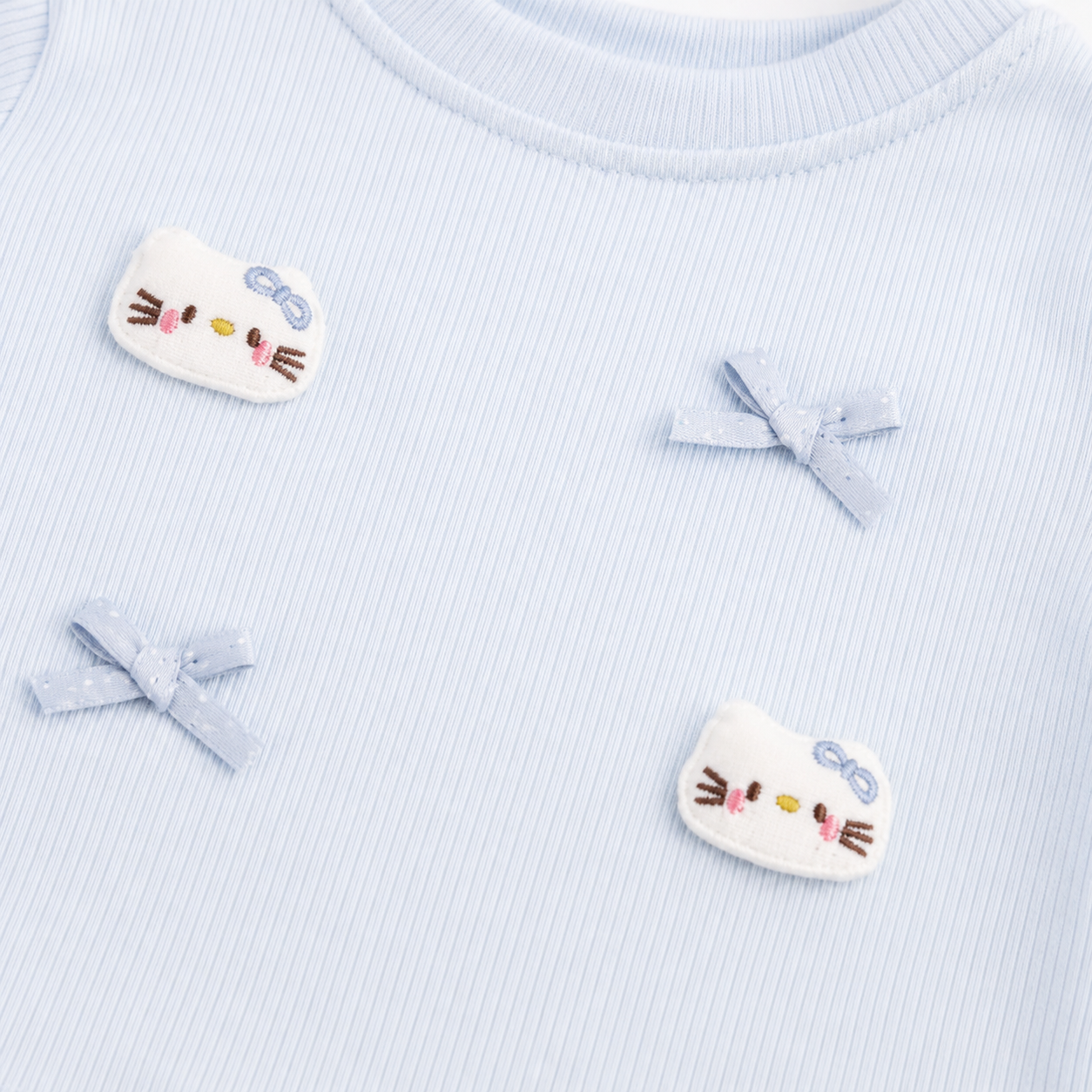 Close-up of the bow applique and patch detail on a light blue girls ruffle top.