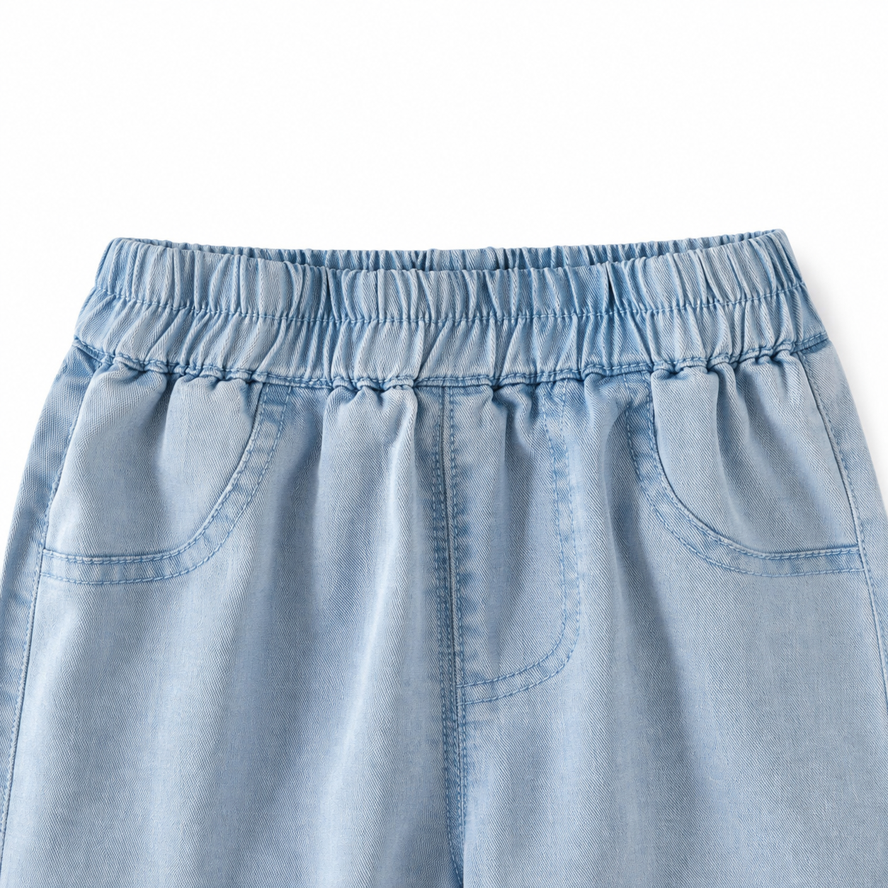 Close-up of the elastic waistband and front pocket details on the light blue girls jeans.