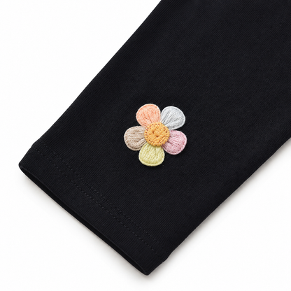 Close-up of the colorful flower applique near the hem of the black leggings.