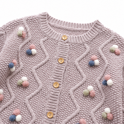 Close-up of the colorful pom blossom details and button-front cable knit design.