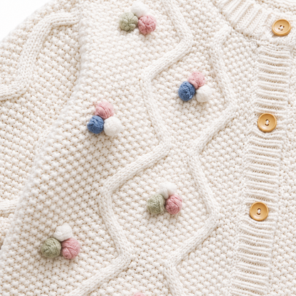 Close-up of the colorful pom blossom details and button-front cable knit design.
