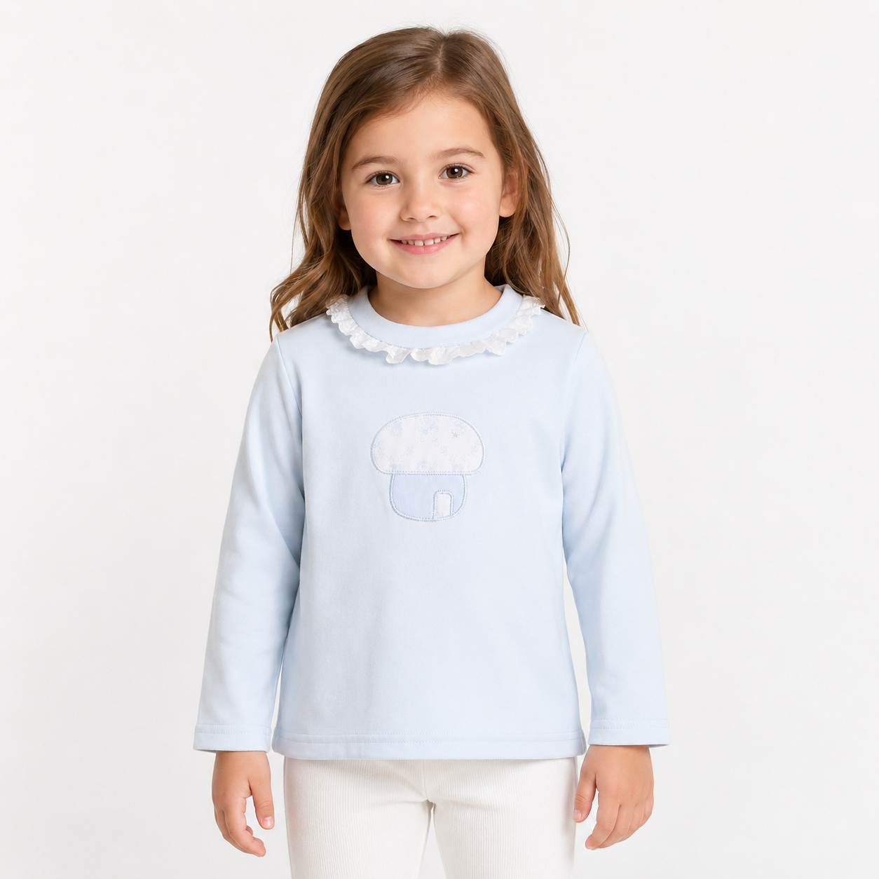 Girl model wearing the Powder Blue cotton long sleeve ruffle collar top with mushroom embroidery on a white studio background.