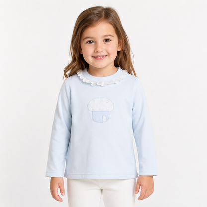 Girl model wearing the Powder Blue cotton long sleeve ruffle collar top with mushroom embroidery on a white studio background.