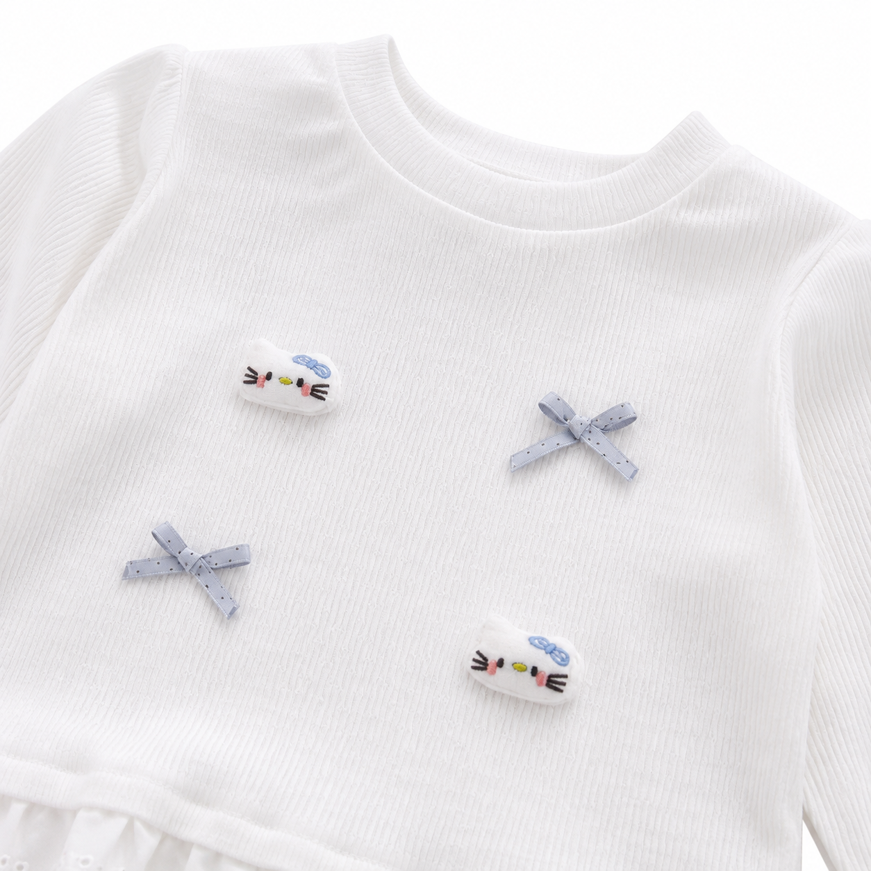 Close-up of the bow applique and patch detail on a white girls ruffle top.