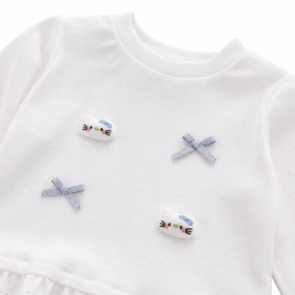 Close-up of the bow applique and patch detail on a white girls ruffle top.