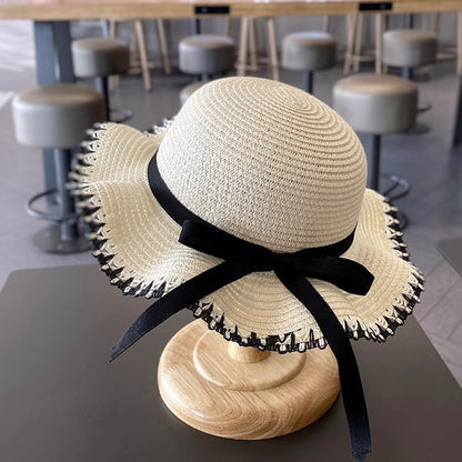 Beige girls straw sun hat with black ribbon bow and scalloped woven brim.