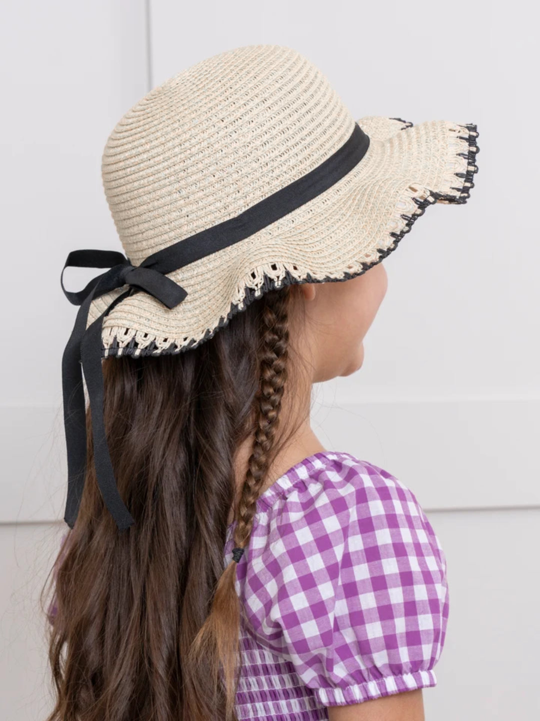 Girl wearing Willow Ribbon Girls Straw Sun Hat with black ribbon bow and scalloped brim.
